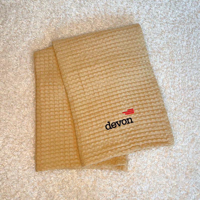 devon balnket - Baby Showers by Mail Cream-colored waffle towel folded on a white surface with a small red-and-black Devon logo.