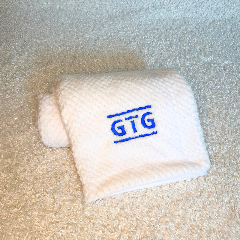 gtg blanket - Baby Showers by Mail White folded towel with blue GTG embroidery on a soft textured surface