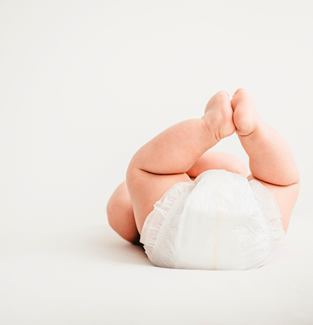 Baby in white clothing holding delicate white baby's breath flowers in front of a light background.